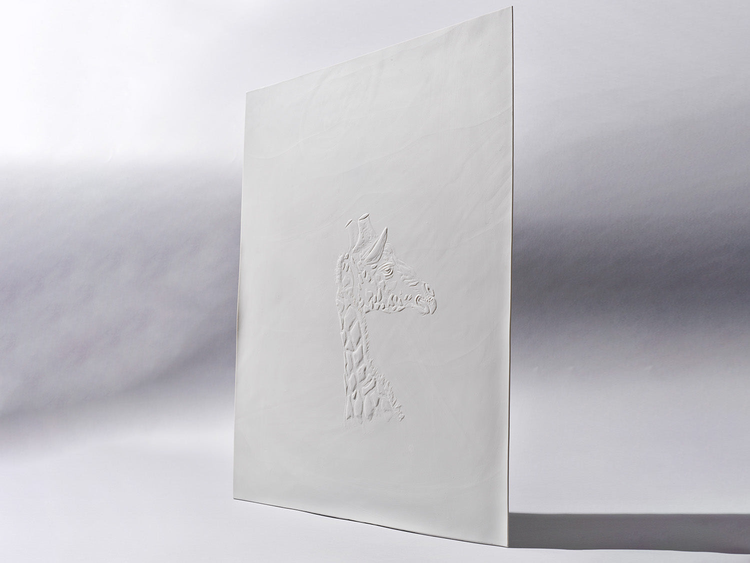 Aufrecht stehende Biskuitporzellanfliese in Weiß mit einem plastisch ausgearbeiteten Giraffenkopf im Profil. Die matte Oberfläche unterstreicht die feine Reliefstruktur.