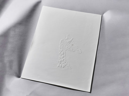 Weiße, matte Biskuitporzellanfliese mit erhabenem Giraffenrelief im Profil. Die flache Fliese liegt auf hellem Untergrund, das Tiermotiv ist fein modelliert.