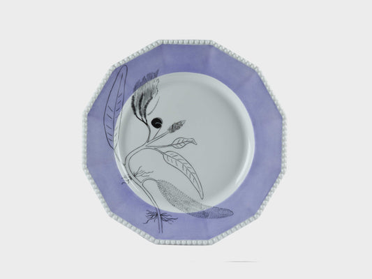 Achteckiger Porzellanteller mit perlförmigem Rand. Der breite Rand ist lavendelfarben glasiert. Im linken Bereich des Tellers ist eine feine, schwarze botanische Zeichnung mit stilisierten Blättern und Samen dargestellt.
Octagonal porcelain plate with a beaded rim. The wide rim is glazed in lavender. A fine black botanical illustration with stylized leaves and seeds is shown on the left side of the plate.