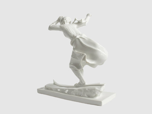 Rückansicht einer weißen Porzellanfigur einer Skifahrerin in Bewegung, mit weit schwingendem Rock auf Skiern, freigestellt vor hellem Hintergrund.
Rear view of a white porcelain figurine of a female skier in motion, with a wide swirling skirt on skis, isolated against a light background.