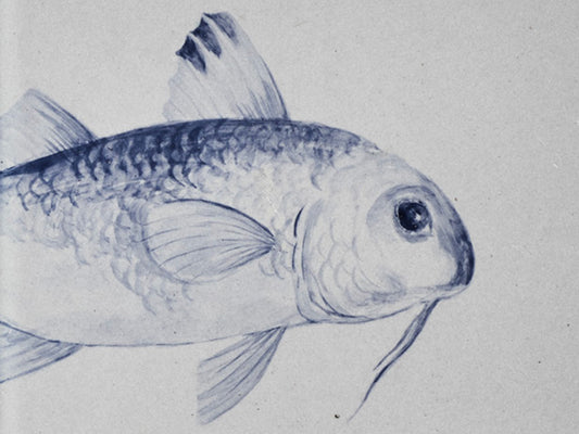 Detailaufnahme einer handbemalten Keramikkachel mit einem in Blau gemalten Fischmotiv.
Close-up of a hand-painted ceramic tile featuring a fish motif painted in blue.