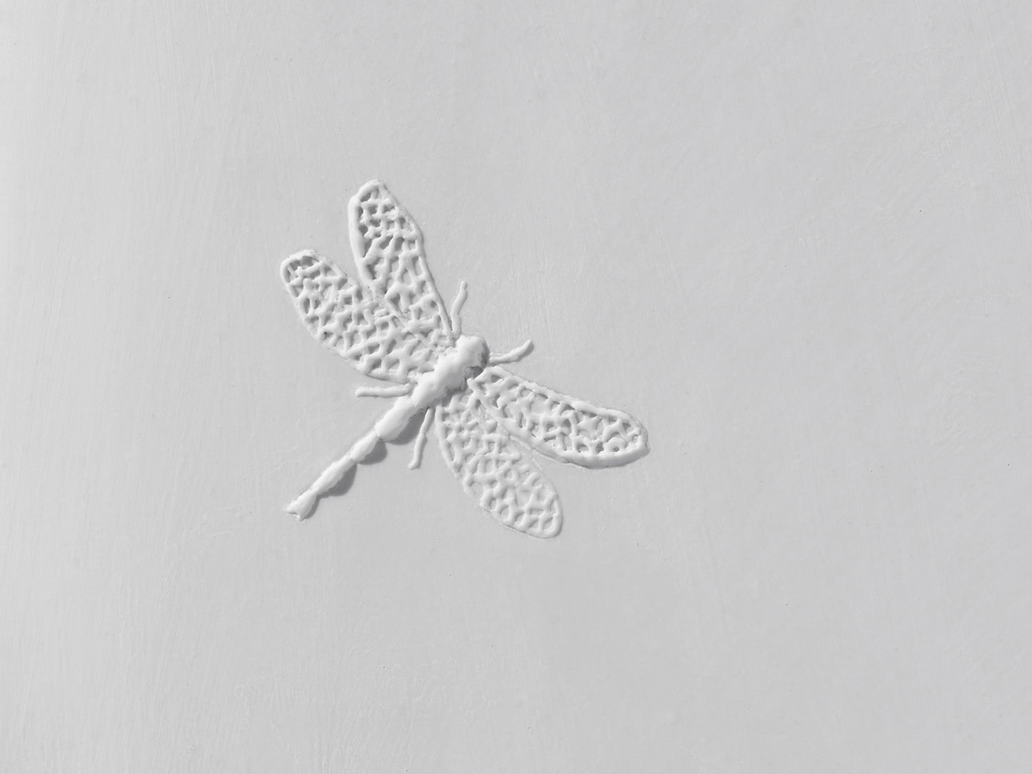 Detailaufnahme des Libellenreliefs auf weißer Biskuitfliese, mit filigraner Flügelstruktur und matter Oberfläche.
Close-up of the dragonfly relief on a white biscuit tile, showing intricate wing structures and a matte surface.