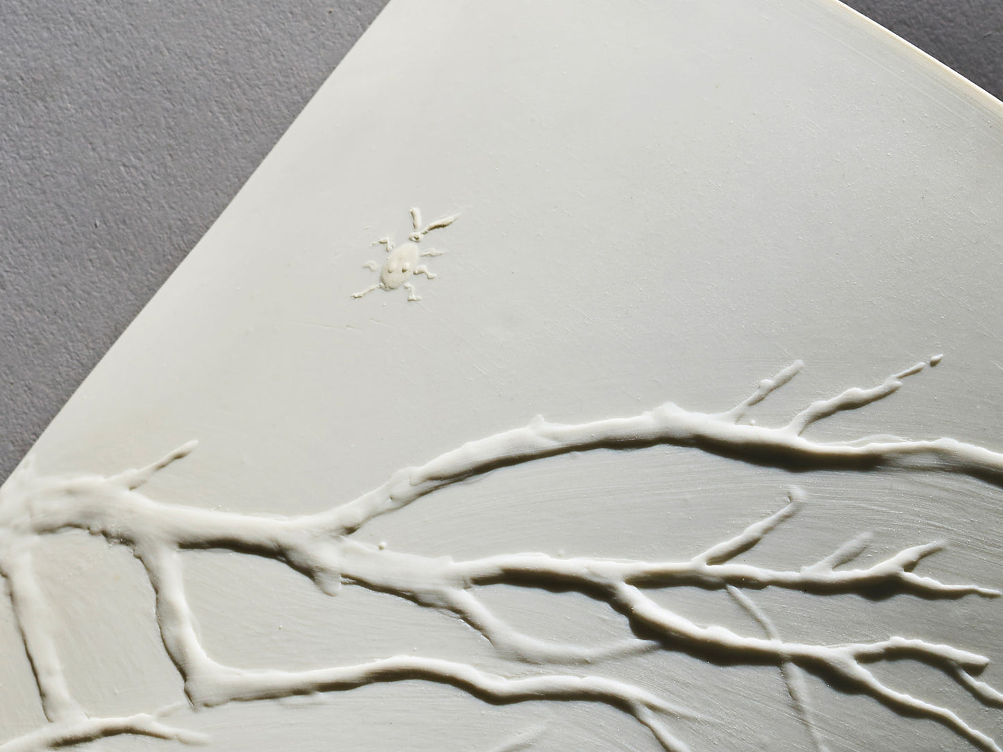 Detailaufnahme des plastischen Zweigreliefs mit Insekt auf weißem Biskuitporzellan.
Close-up of sculpted branch relief with insect on white biscuit porcelain.