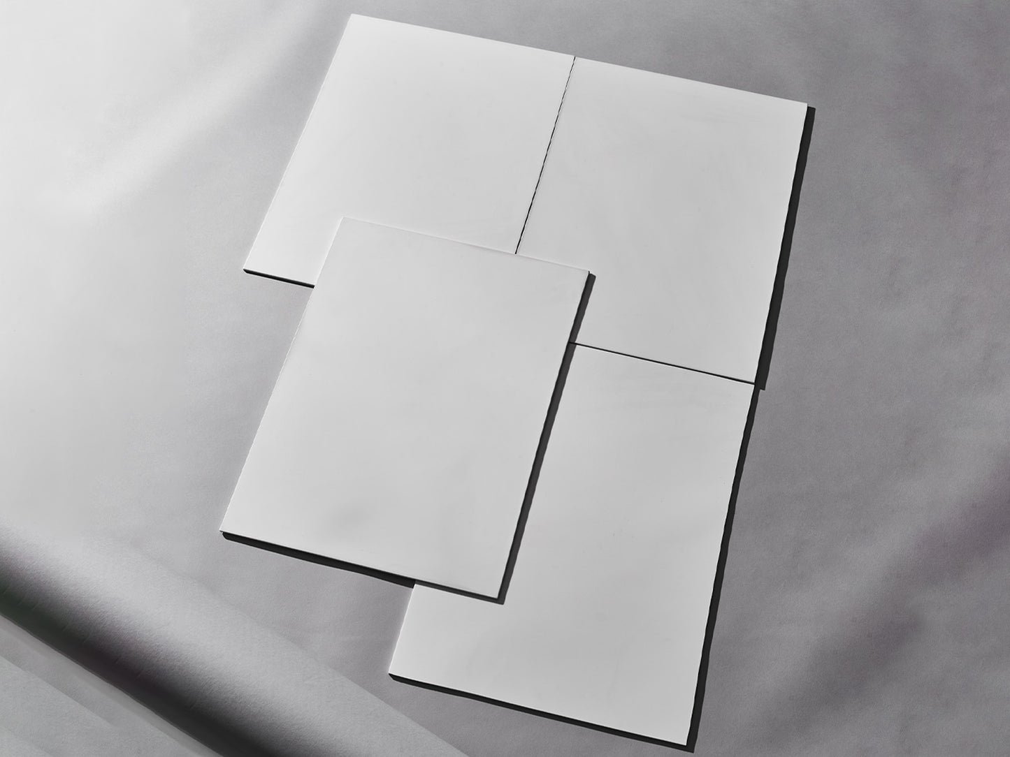 Vier weiße Fliesen auf grauem Hintergrund arrangiert.
Four white tiles arranged on grey background.