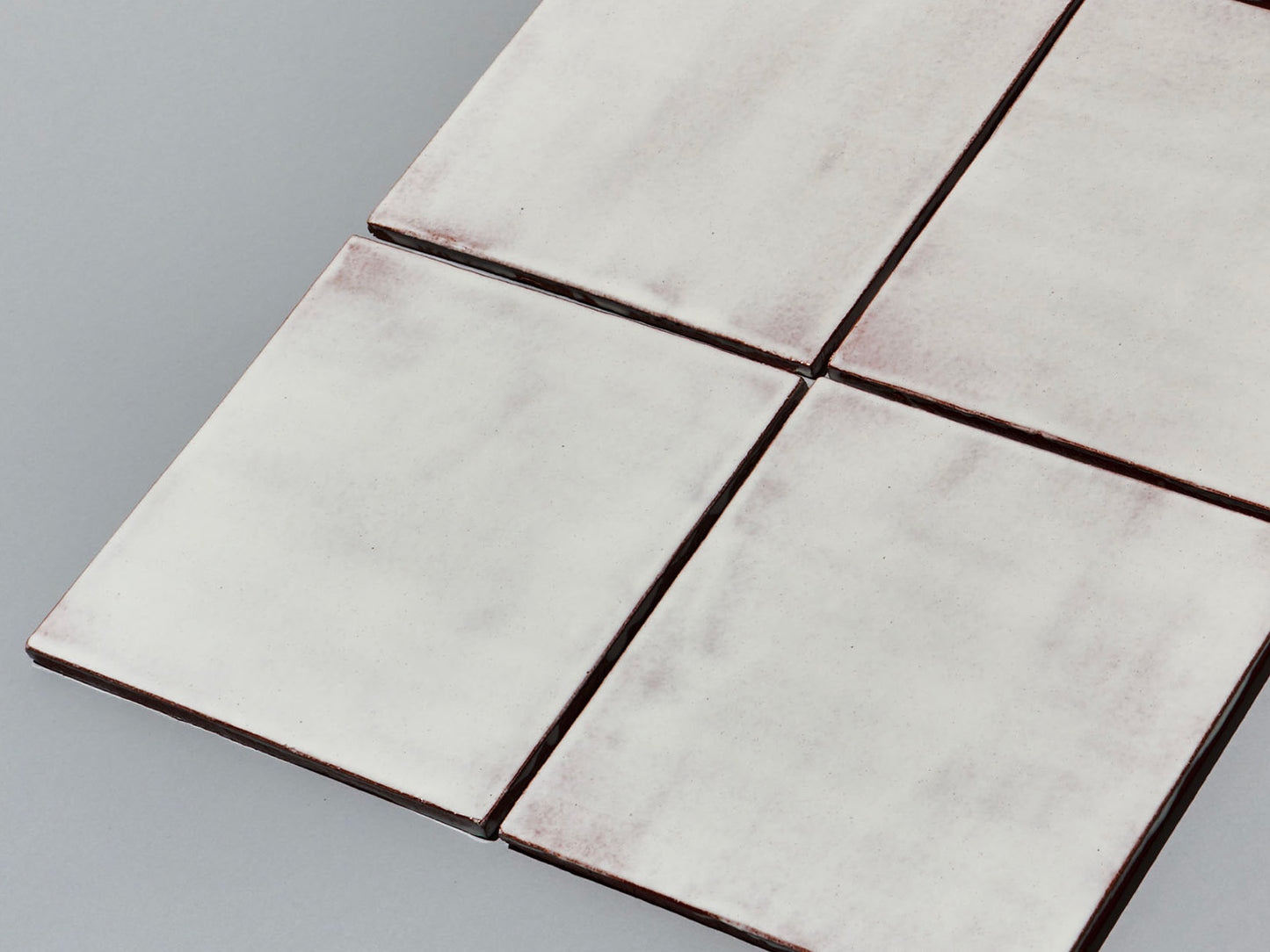 Vier Majolika-Fliesen mit durchschimmernder weißer Glasur in Fugenanordnung.
Four majolica tiles with translucent white glaze arranged with fine grout lines.