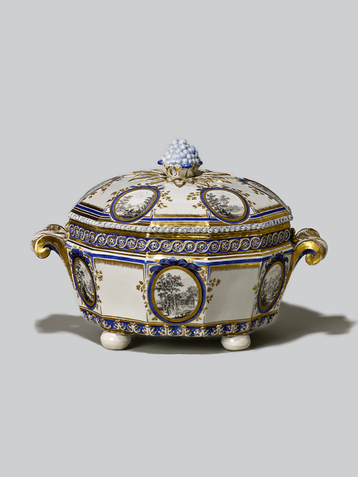 Porzellan-Terrine mit kobaltblauer und goldener Verzierung, Landschaftsmedaillons in Grisaille und plastischem Traubenknauf auf dem Deckel, Serie „Perl“.
Porcelain tureen with cobalt blue and gold decoration, grisaille landscape medallions and sculptural grape finial on the lid, “Perl” series.
