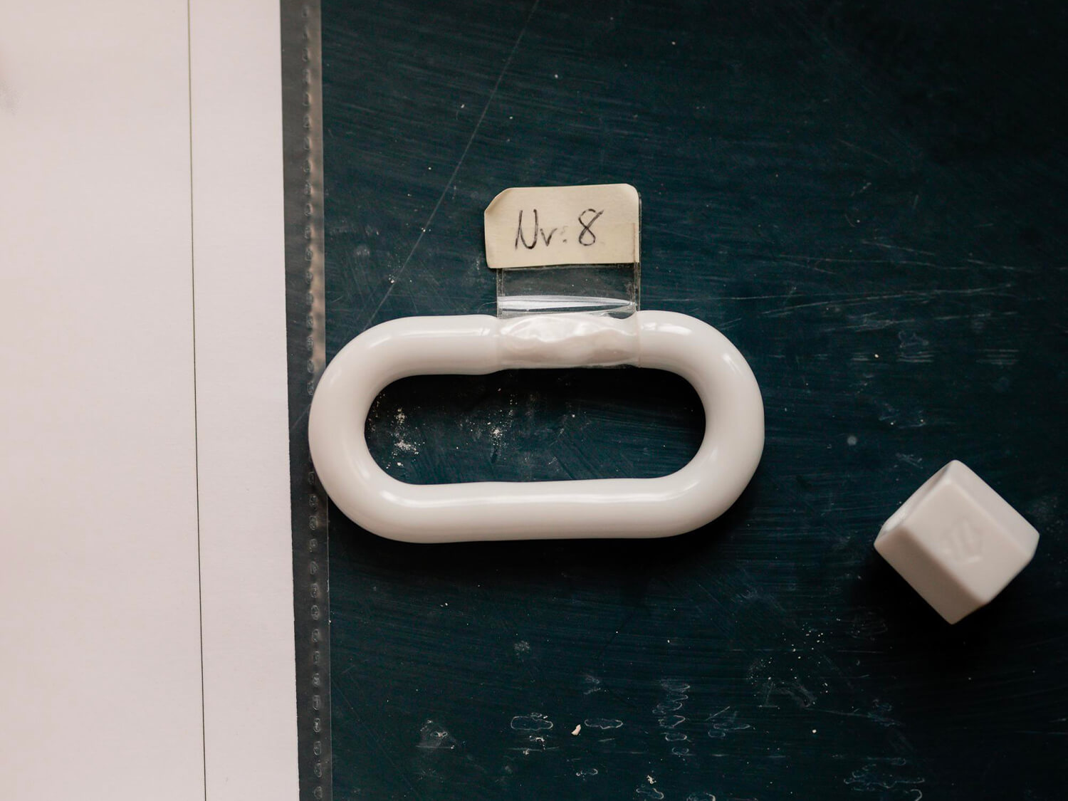 Unbemaltes Porzellan-Glied („Lock“) aus der Werkstatt, weiß glasiert, mit Testetikett „Nr. 8“.

Unpainted porcelain lock blank from the workshop, white-glazed, labeled “No. 8”.