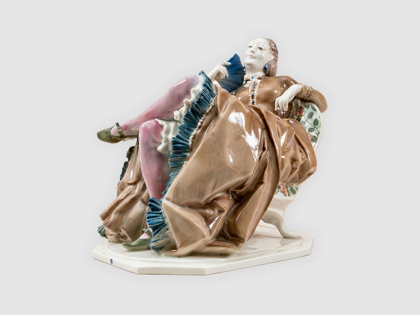 Polychrome Porzellanfigur einer entspannt zurückgelehnten Dame im Sessel mit voluminösem, braun glasiertem Kleid, rosa Strümpfen und blauem Fächer.

Polychrome porcelain figurine of a reclining lady in an armchair with a voluminous brown glazed dress, pink stockings and a blue fan.