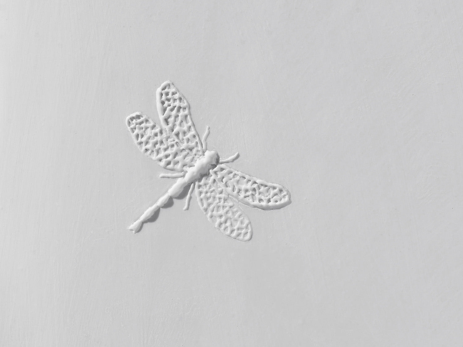 Detailaufnahme des Libellenreliefs auf weißer Biskuitfliese, mit filigraner Flügelstruktur und matter Oberfläche.

Close-up of the dragonfly relief on a white biscuit tile, showing intricate wing structures and a matte surface.