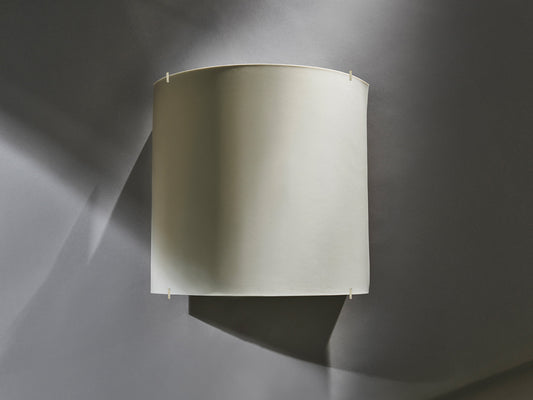 Wandleuchte aus unglasiertem Biskuitporzellan mit schlichter, gewölbter Form vor grauer Wand, unbeleuchtet.

Wall light made of unglazed biscuit porcelain with a simple, curved form mounted on a grey wall, unlit.