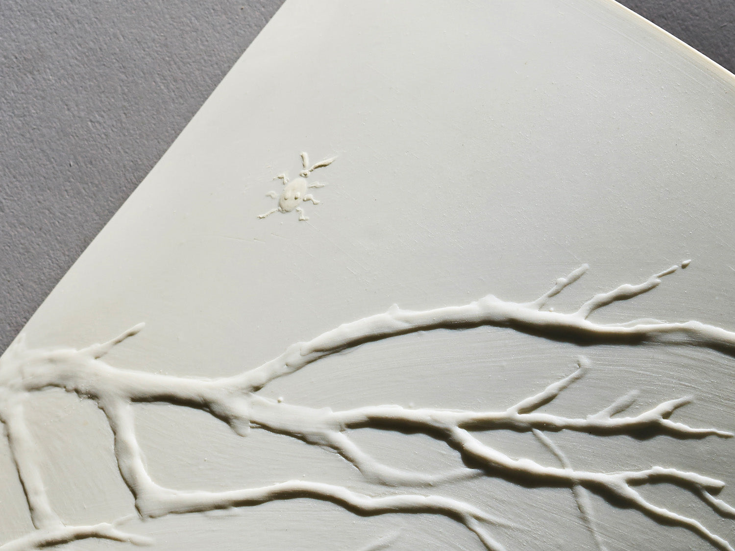 Detailaufnahme des plastischen Zweigreliefs mit Insekt auf weißem Biskuitporzellan.

Close-up of sculpted branch relief with insect on white biscuit porcelain.