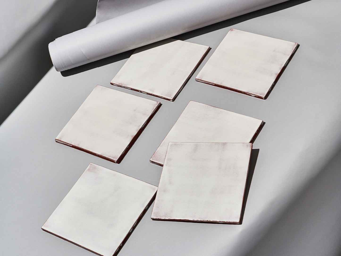 Sechs Majolika-Fliesen mit weißlich-transparenter Glasur „White Frosting“ auf grauem Untergrund arrangiert.

Six majolica tiles with semi-transparent white “White Frosting” glaze arranged on a grey background.