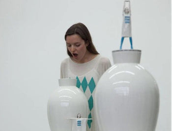 Eine Stimmbildnerin spricht bei einer Kunstaktion in Porzellanvasen 
A vocal coach speaks into porcelain vases during an art performance.