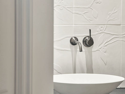 Badezimmerwand mit Kirschblütenrelieffliesen hinter einem modernen Waschbecken.
Bathroom wall with cherry blossom relief tiles behind a modern washbasin.